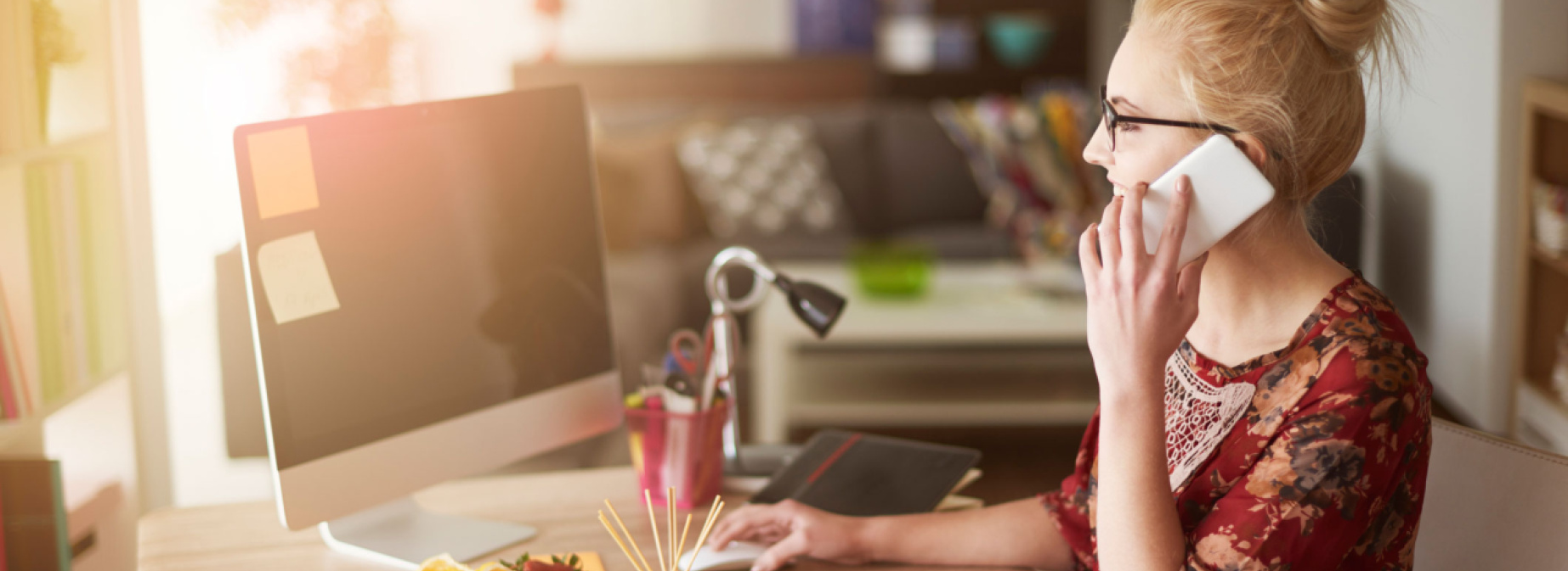 Young woman sitting at the desk and looking at a computer screen while talking on the phone