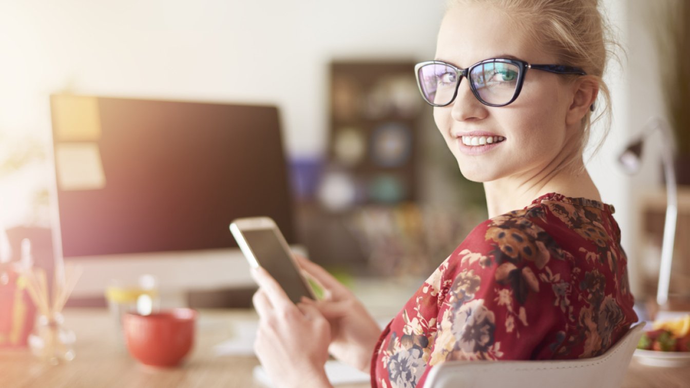 Young woman with smartphone in her hand is smiling at the camera