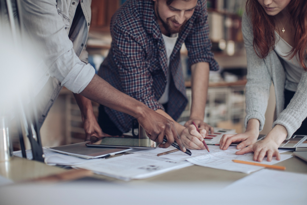 Group of people standing around a table and discussing a stack of strategy papers