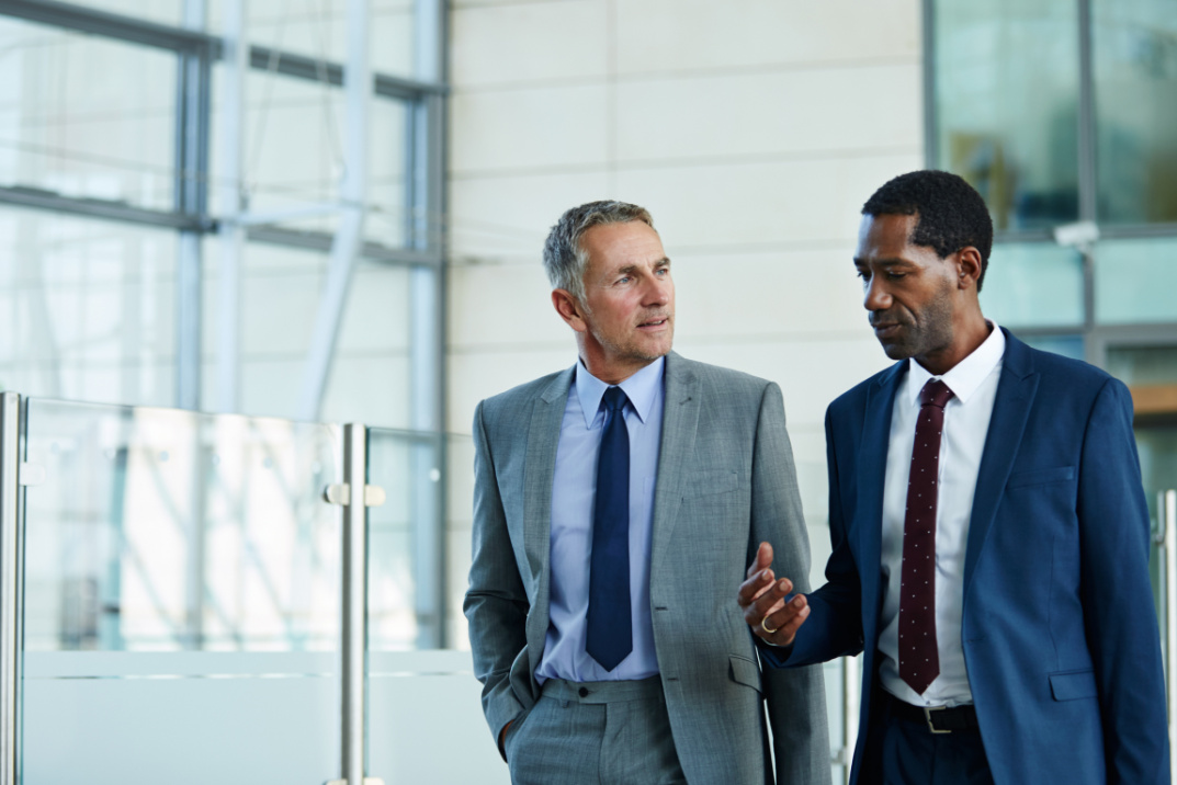 Two men in suits walking through a modern office building while discussing