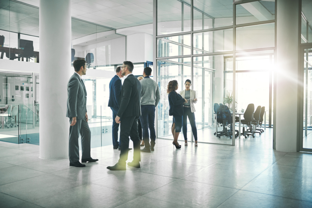 Gruppe von Menschen in Anzügen steht vor einem modernen Büro und disktuiert